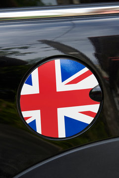 Closeup of a round refueling cap with a design of the national flag of Great Britain, surrounded by black shiny auto paint and chrome parts