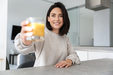 Image of beautiful woman 30s drinking orange juice, while resting in bright modern room