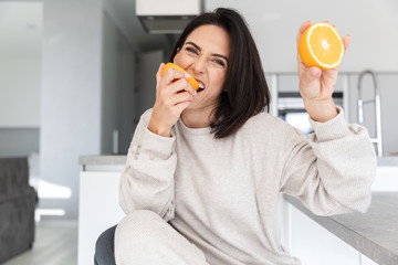Fototapeta premium Image of attractive woman 30s holding two pieces of orange, while sitting in living room