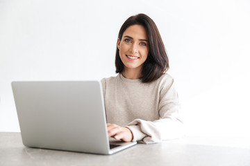 Image of adorable woman 30s working on laptop, while sitting over white wall in bright room