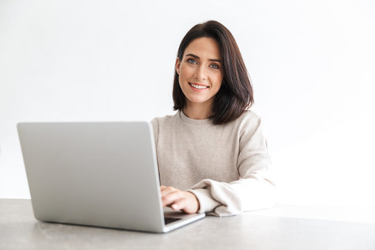 Image Of Adorable Woman 30s Working On Laptop, While Sitting Over White Wall In Bright Room