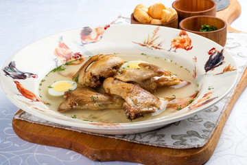 Quail broth with crackers and herbs on a wooden board. On white background.