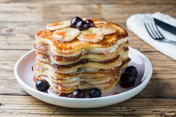 Pancake cake with bananas and berry syrup, selective focus, dark background.
