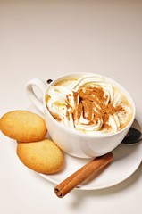 Close up of a hot cup of cappuccino with biscuits and cinnamon stick as decoration on white background. Vertical view, copy text