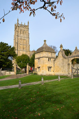 Fototapeta premium Autumn sunshine on the picturesque church and gatehouses in Chipping Campden, a Cotswolds travel destination, Gloucestershire, UK