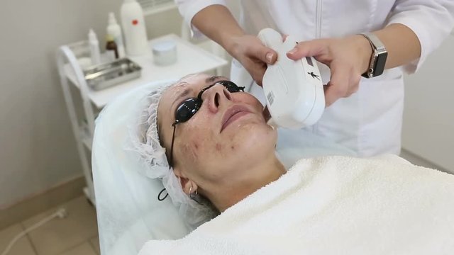 Woman in black glasses getting photo rejuvenation procedure in cosmetology clinic or beauty salon. Beautician doing facial procedure, Skin care concept for middle-aged woman.