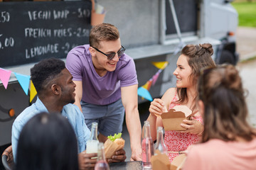 leisure and people concept - happy friends with drinks eating and talking at food truck