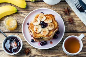 Pancake cake with bananas and berry syrup, selective focus, dark background.