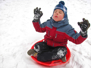 Fototapeta na wymiar Little boy in a winter warm clothes sits in on red sled in a pose of meditation. Portrait.