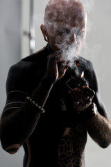 Fototapeta na wymiar handsome shirtless man with tattoos smoking cigar on grey