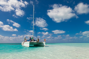 Group of unidentified tourists travel on a catamaran near the island of Kayo Largo.  White catamaran on a background of blue sky and azure water - obrazy, fototapety, plakaty