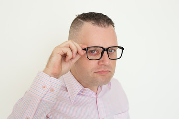 Serious suspicious office employee touching temple of eyeglasses. Closeup of young Caucasian man...