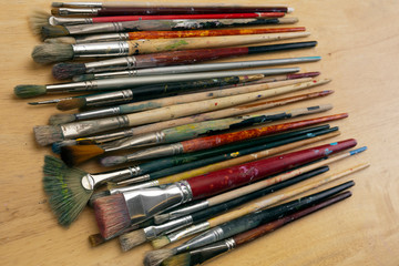 A collection of well used art paint brushes on wood