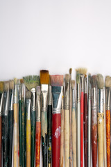 Fototapeta premium A collection of well used art paint brushes on white paper surface