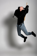 Fototapeta na wymiar aggressive bald man in leather jacket holding baseball bat and jumping on grey