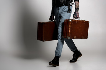 low section of tattooed man in leather jacket walking with suitcases on grey