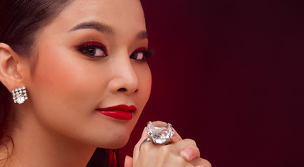 Beautiful Young Asian black hair fur woman in fire red screen, high glitter fashion make up, studio lighting hot smoke burgundy background copy space, concept empty Big Karat Diamond Ring expensive