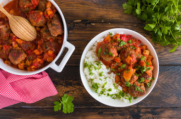 Moroccan meatballs in a spicy sauce with tomatoes and dried apricots and boiled rice. White casserole and bowl on wooden rustic table, top view