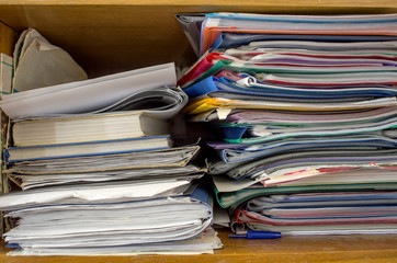 On the bookshelf closely stacked books, folders, papers, brochures into two piles.