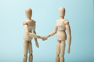 Two wooden figures of man shake hands.