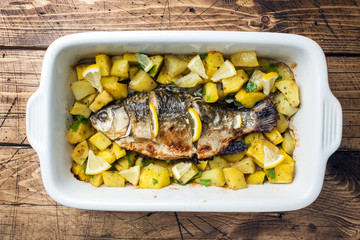 Baked fish carp with potatoes in a ceramic pan. Rustic style.