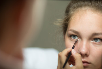 Mirror reflection of young woman making up her eye