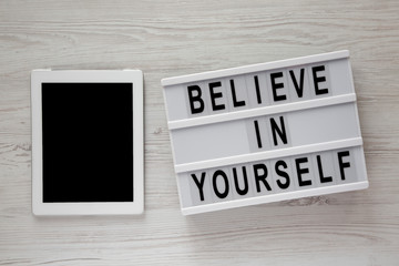 Lightbox with text 'Believe in yourself', tablet on a white wooden background, top view. From above, flat lay, overhead.