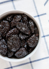 Full bowl of dry prunes on cloth, overhead view. Flat lay, from above, top view.