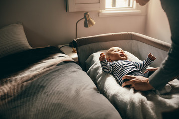 Woman putting her baby in a bedside crib