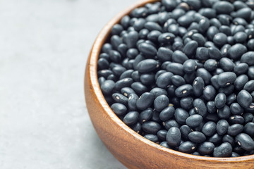 Black beans in wooden bowl on gray concrete background, horizontal, copy space