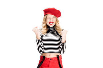 cheerful woman in red beret smiling while celebrating winning isolated on white