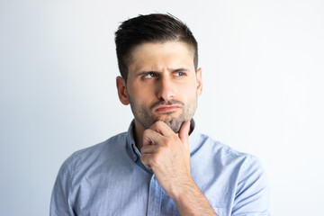 Pensive frowning guy in casual making decision. Young Caucasian man with stubble touching and scratching chin and staring into vacancy. Thinking concept