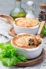 Vegetarian pot pie with lentil, mushroom, potato, carrot and green peas, covered with puff pastry, in a baking dish, vertical