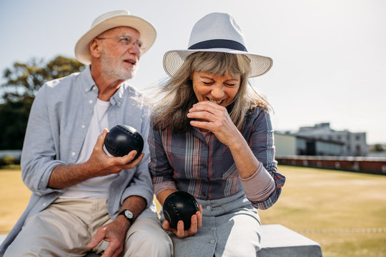 Elderly couple having fun sitting at a park holding boules