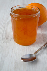 Homemade orange marmelade in glass jar on a white wooden background, side view.