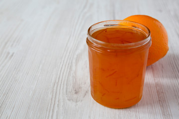 Homemade orange marmelade in glass jar on a white wooden surface, side view. Copy space.