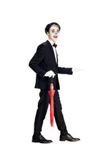 cheerful clown in suit and black beret holding umbrella while walking isolated on white