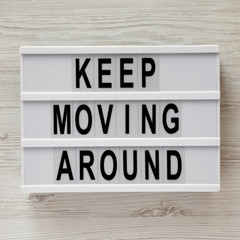 Lightbox with text 'Keep moving around' over white wooden background, overhead view. From above, flat lay, top view.