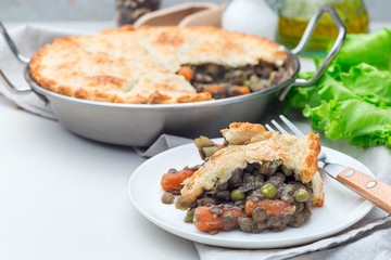 Vegetarian pot pie with lentil, mushrooms, potato, carrot and green peas, covered with puff pastry, on white plate, horizontal, copy space