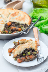 Vegetarian pot pie with lentil, mushrooms, potato, carrot and green peas, covered with puff pastry, on white plate, vertical
