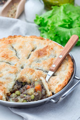 Vegetarian pot pie with lentil, mushrooms, potato, carrot and green peas, covered with puff pastry, in a baking dish, vertical