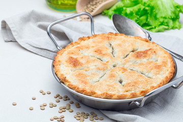 Vegetarian pot pie with lentil, mushrooms, potato, carrot and green peas, covered with puff pastry, in a baking dish, horizontal
