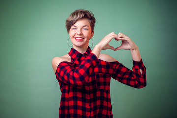 Fototapeta premium People and emotions -a portrait of smiling young woman with short hair showing with her finger heart figure