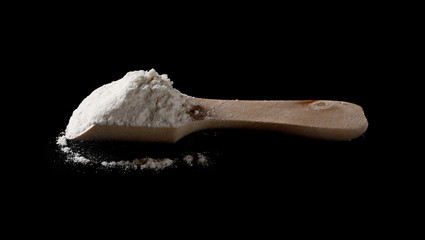 Wheat flour pile in wooden spoon isolated on black background, powder texture