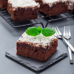 Homemade brownie with coconut flakes, swedish dessert Karleksmums, cut in square servings, on a stone plate and cooling rack, square format