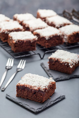 Homemade brownie with coconut flakes, swedish dessert Karleksmums, cut in square servings, on stone plate and cooling rack, vertical