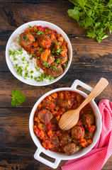 Moroccan meatballs in a spicy sauce with tomatoes and dried apricots and boiled rice. White casserole and bowl on wooden rustic table, top view