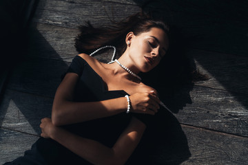 Top view portrait of beautiful young brunette woman with closed eyes in black dress lying om wooden floor
