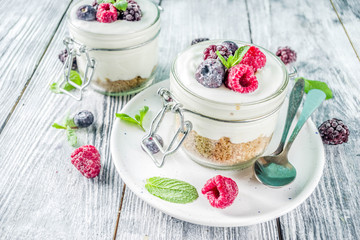 Recipe ideas for summer diet breakfast, healthy morning dessert Cheesecake in portioned jars with summer berries - raspberry, blueberry, blackberry. On wooden background copy space