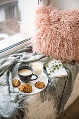 Fototapeta premium Scandinavian style breakfast, cup of coffee and cookies on cozy windowsill with warm blanket and pillow